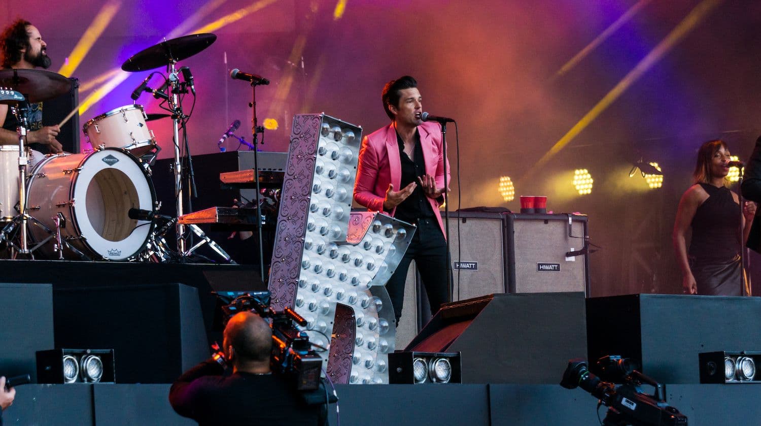 Brandon Flowers of The Killers performing on stage beside a giant light-up K sign